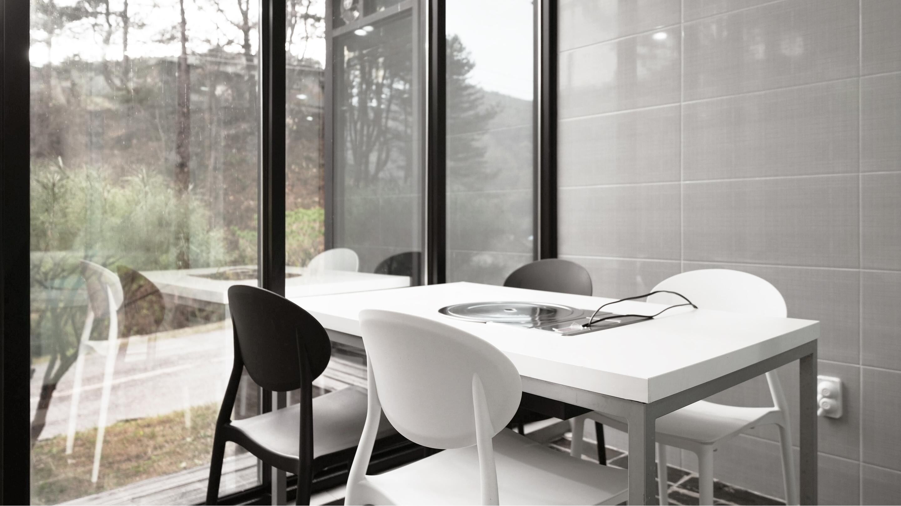 Un comedor moderno con una mesa y sillas blancas, ventanas amplias y vistas a árboles.