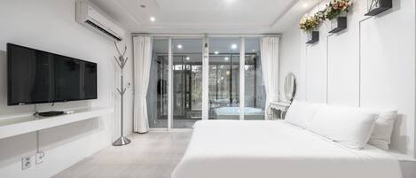 A modern bedroom with a large bed, a flat-screen TV mounted on the wall, and a glass door leading to a balcony.
