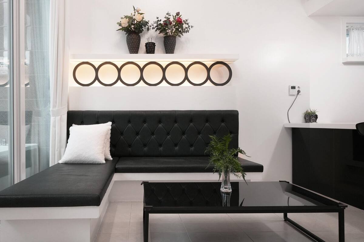 Un salon moderne avec un canapé noir, une table basse en verre et un luminaire fixé au mur.