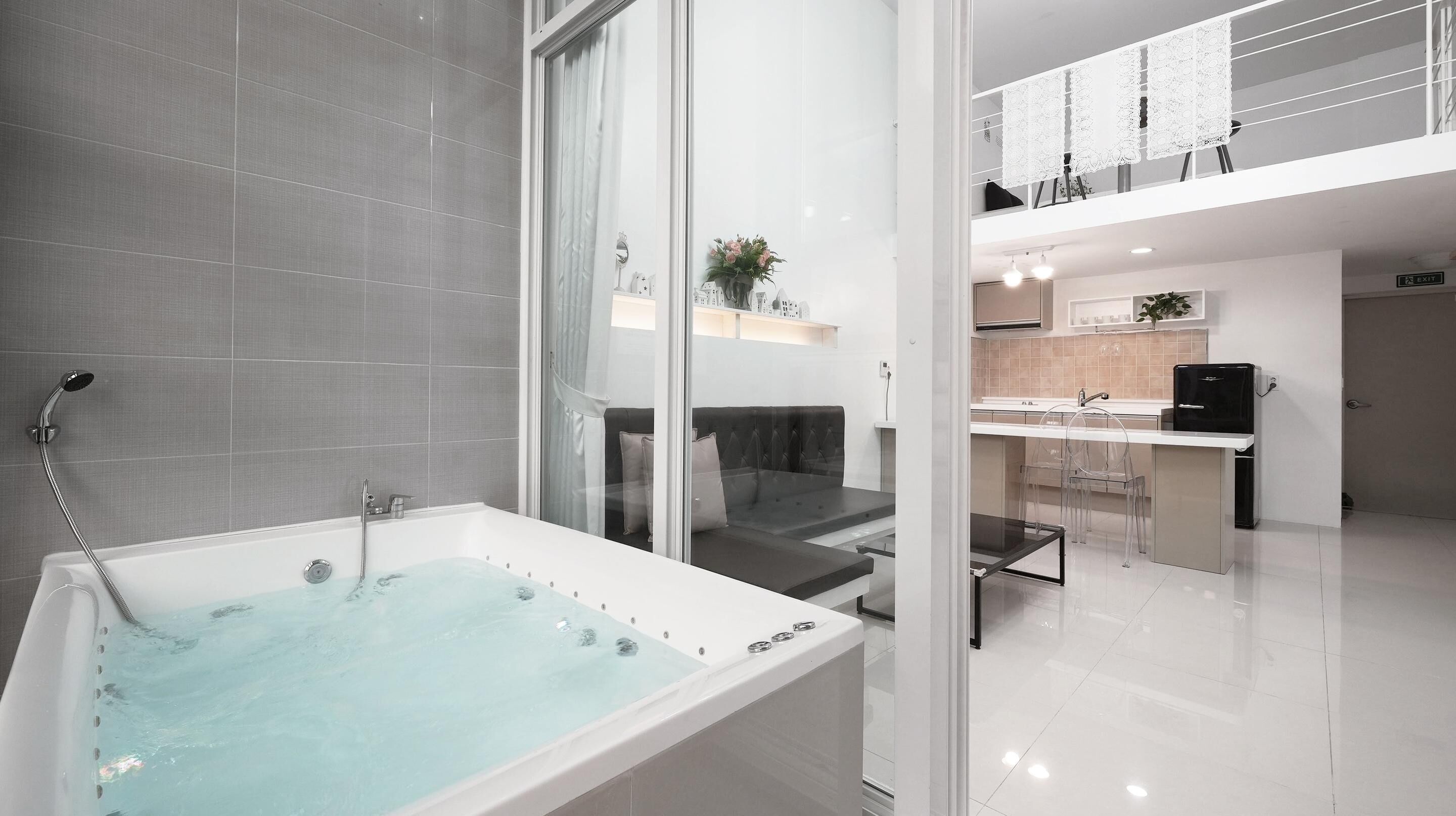 Une salle de bain moderne dotée d’une baignoire, d’une douche à parois de verre et d’un espace détente avec un canapé et des fauteuils.