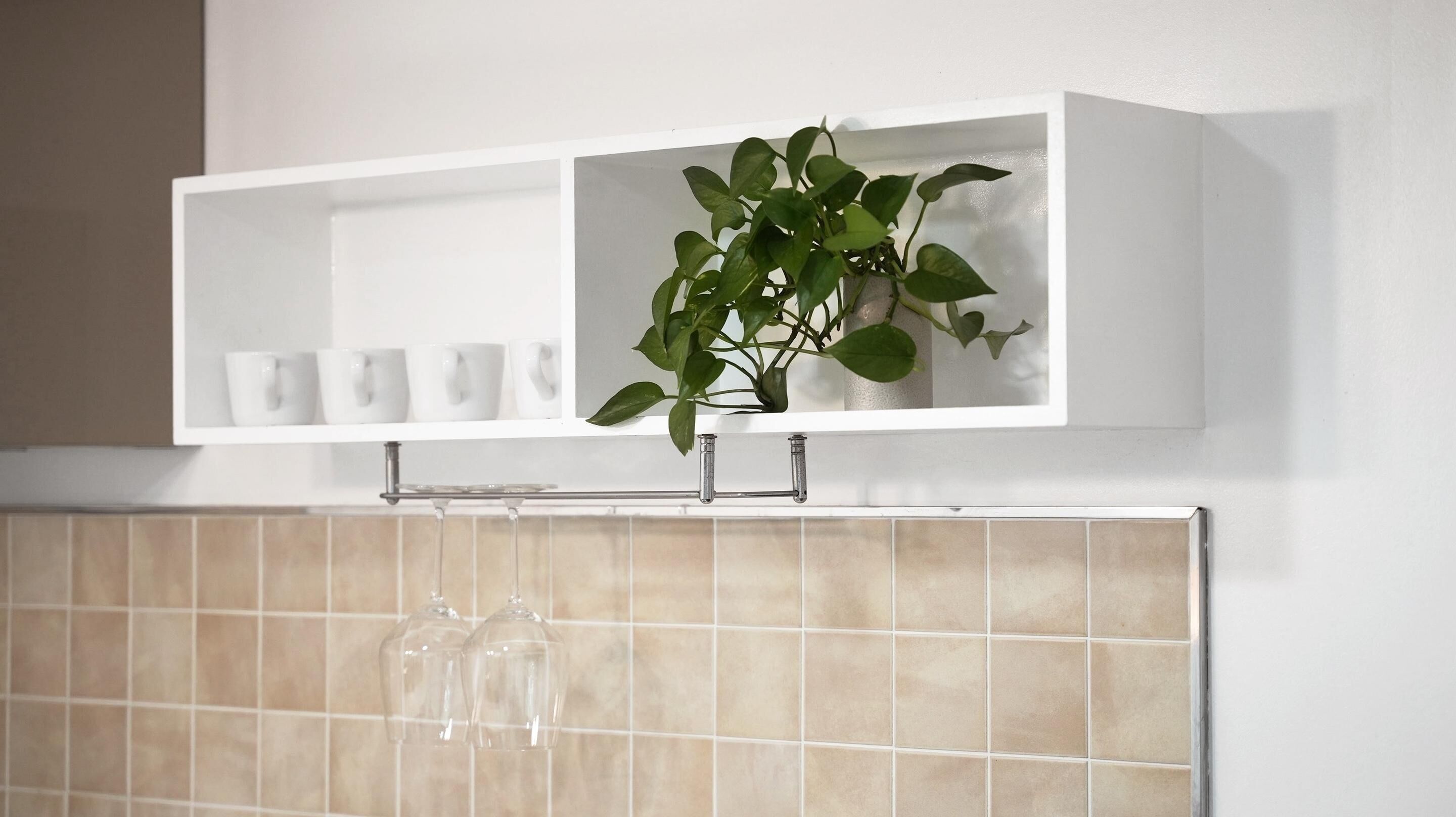 A bathroom with a white shelf holding white cups and a potted plant.