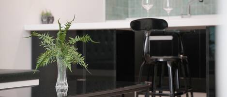 A modern kitchen with a glass table, a clear vase with green plants, and black chairs.