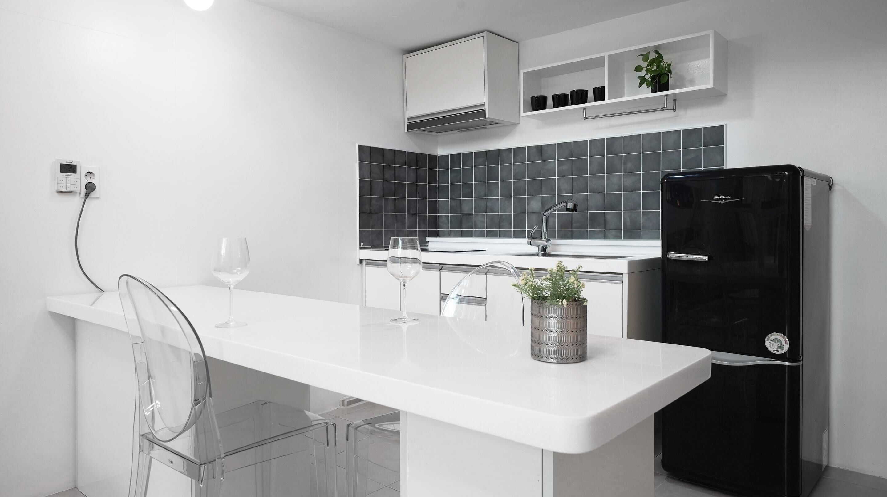 Una cocina moderna con encimera blanca, refrigerador negro y salpicadero gris.
