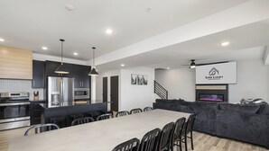 Een moderne keuken met roestvrijstalen apparatuur, een eethoek met een grote tafel en stoelen, en een zithoek met een bank en een open haard.