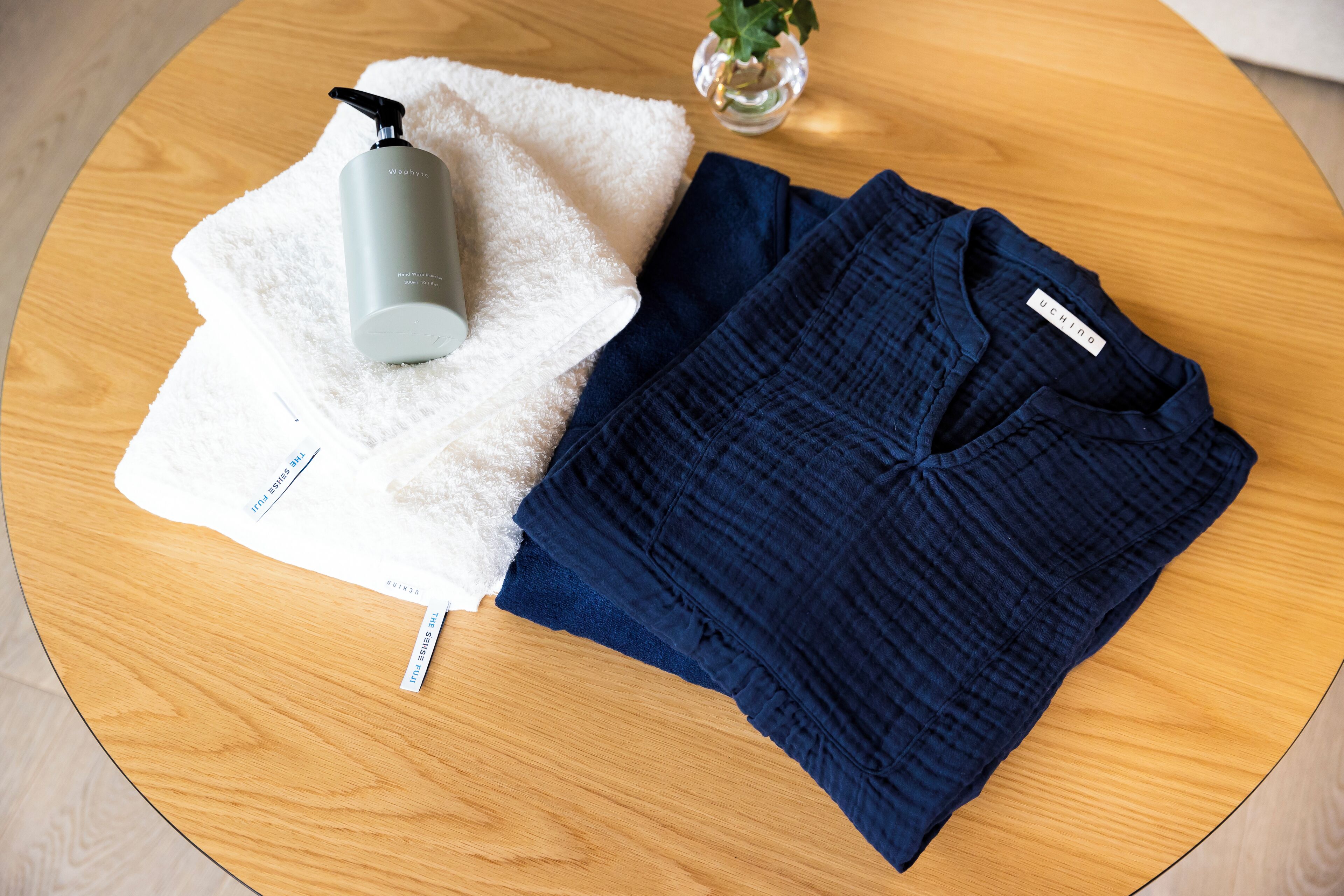A round wooden table with a white towel, a grey bottle, and a dark blue shirt with a label.