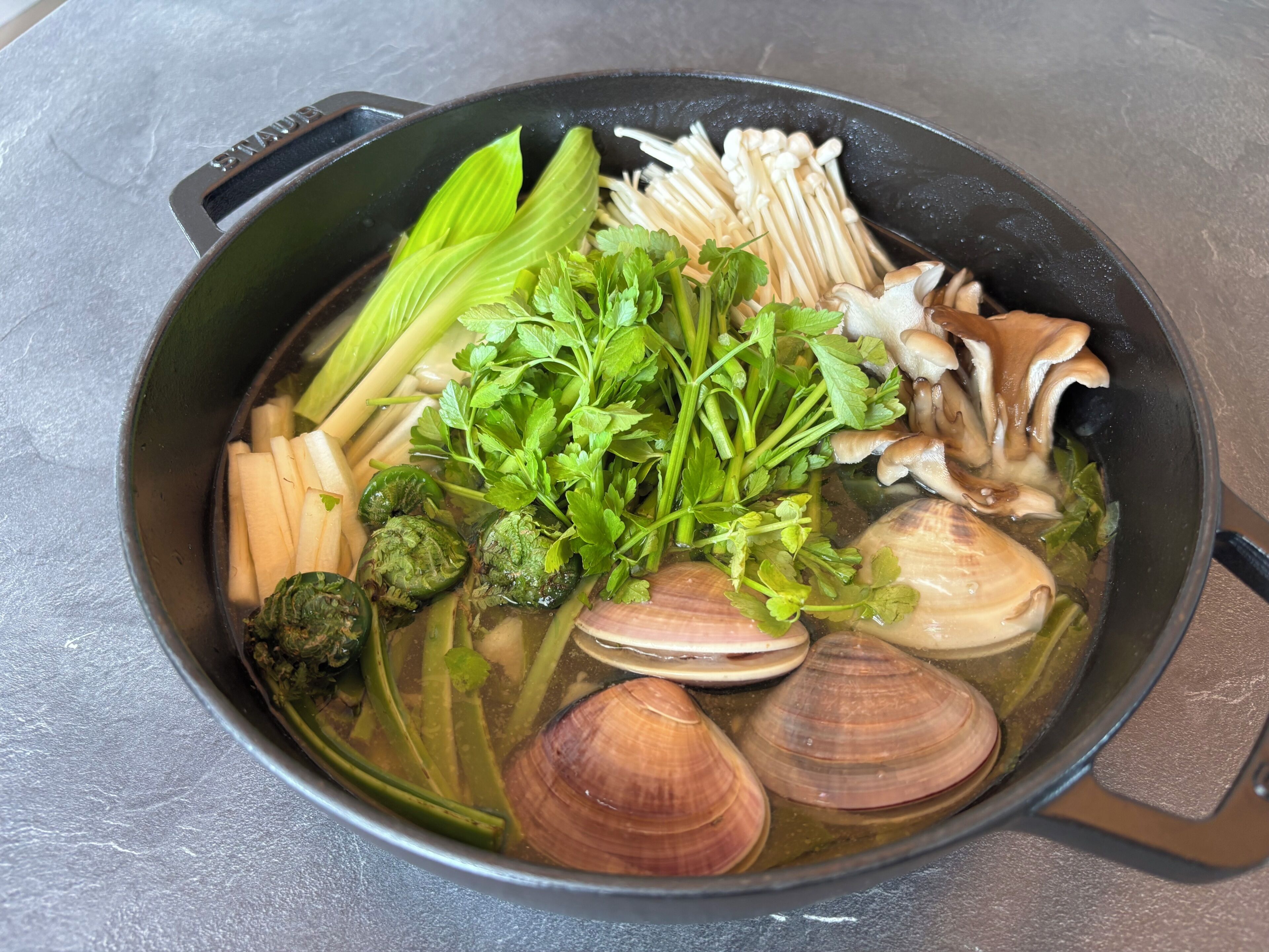 Une marmite contenant divers légumes et des palourdes.