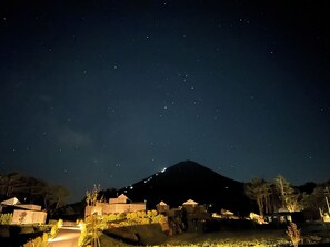 Cielo nocturno con estrellas, una montaña y un edificio iluminado con un sendero que lo lleva a él.