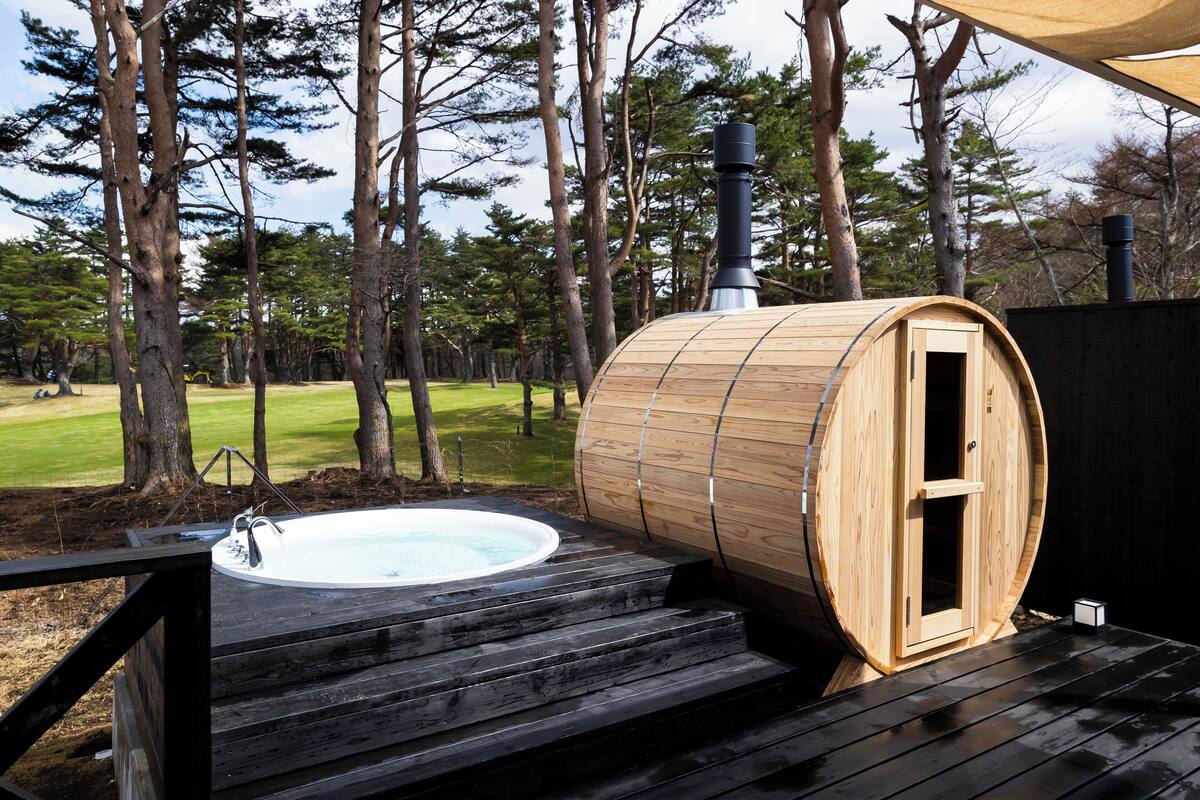 A sauna with a wooden exterior and a hot tub on a wooden deck, surrounded by trees.