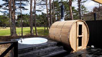 A sauna with a wooden exterior and a hot tub on a wooden deck, surrounded by trees.
