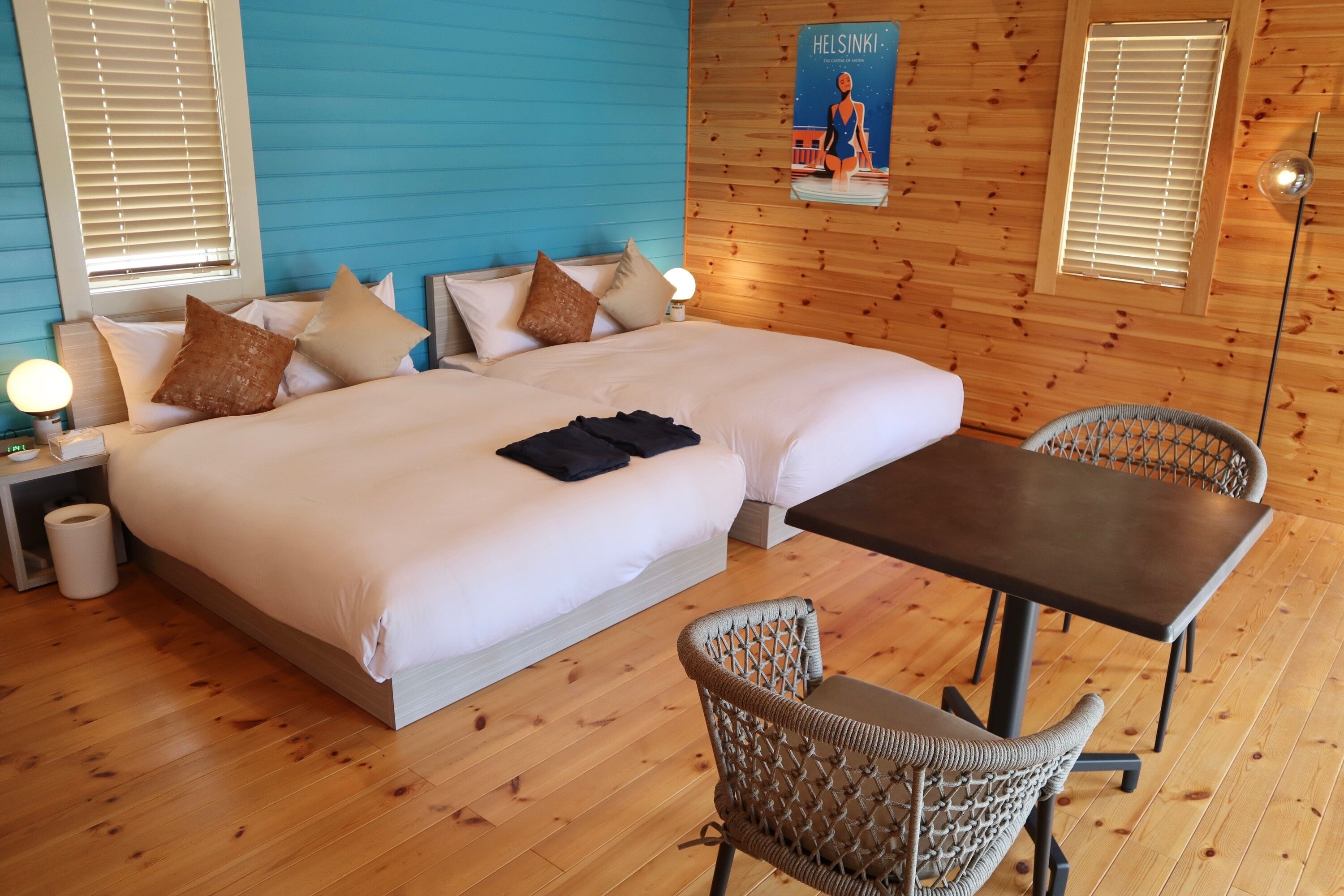A room with two beds, a table, wicker chairs, and a poster on the wall.