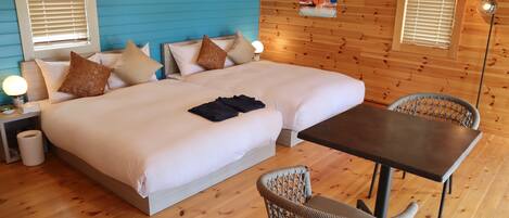 A room with two beds, a table, wicker chairs, and a poster on the wall.