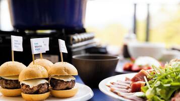 A table with three mini burgers on a plate, a bowl of salad, and a grill in the background.