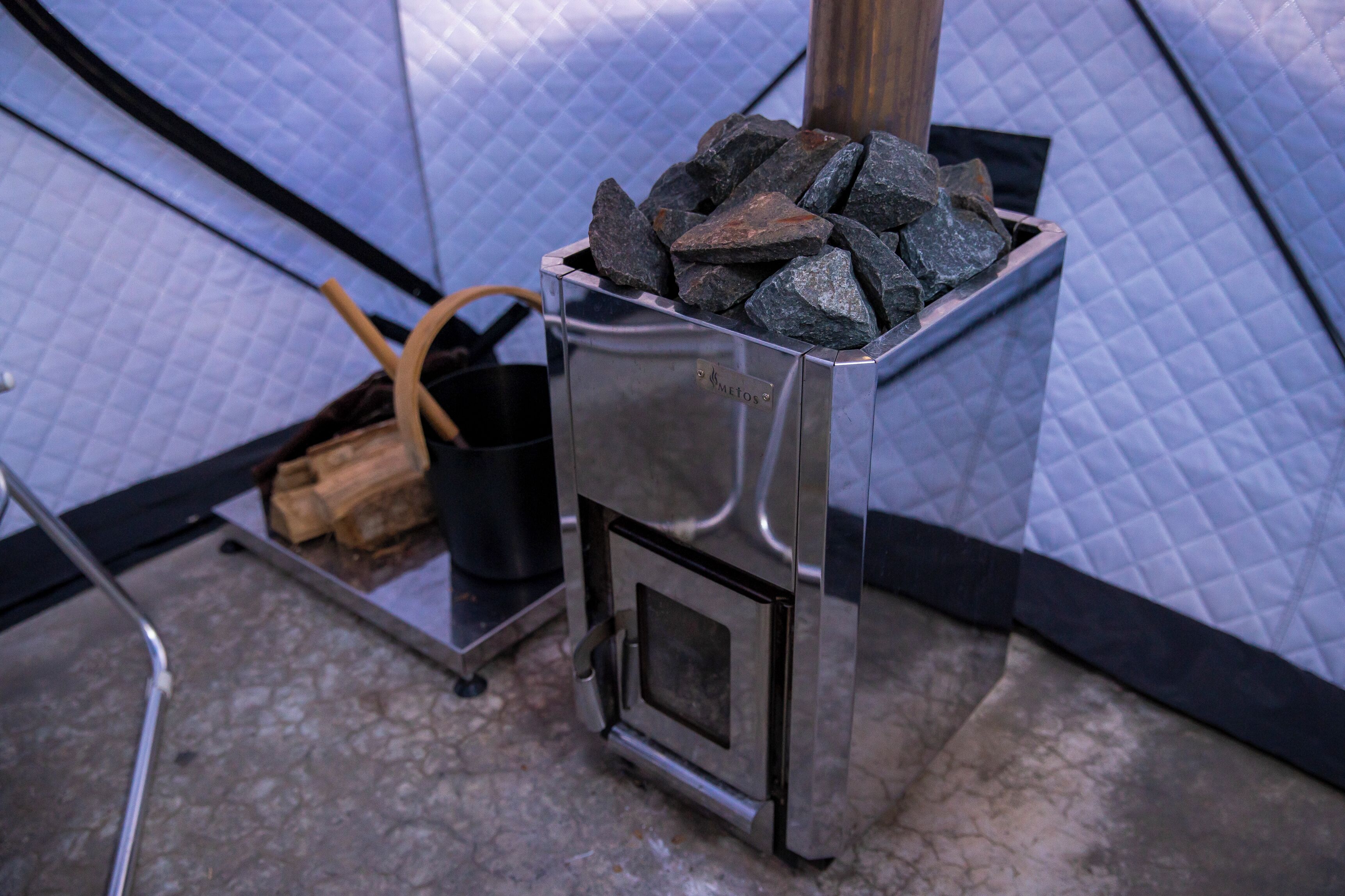 A metal stove with a metal container filled with rocks, a metal bucket, and a wooden handle.