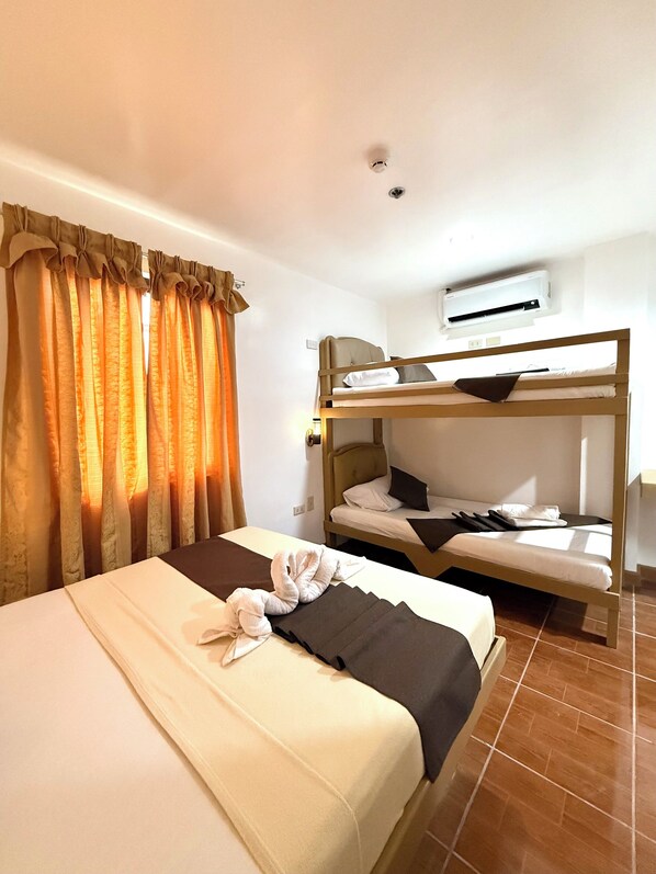 Una habitación de hotel con literas, una cama individual, una ventana con cortinas, un equipo de aire acondicionado y suelo de baldosas.
