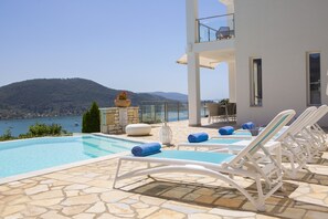 A pool area with lounge chairs and a view of the sea.