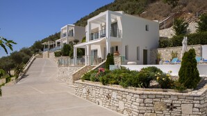Un bâtiment moderne à deux étages, doté de balcons, de murs en pierre et d’un jardin aménagé avec diverses plantes et fleurs.