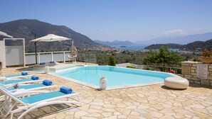 Une piscine sur le toit, avec une eau d’un bleu cristallin, entourée de carreaux de pierre, et offrant une vue panoramique sur les montagnes et la mer.