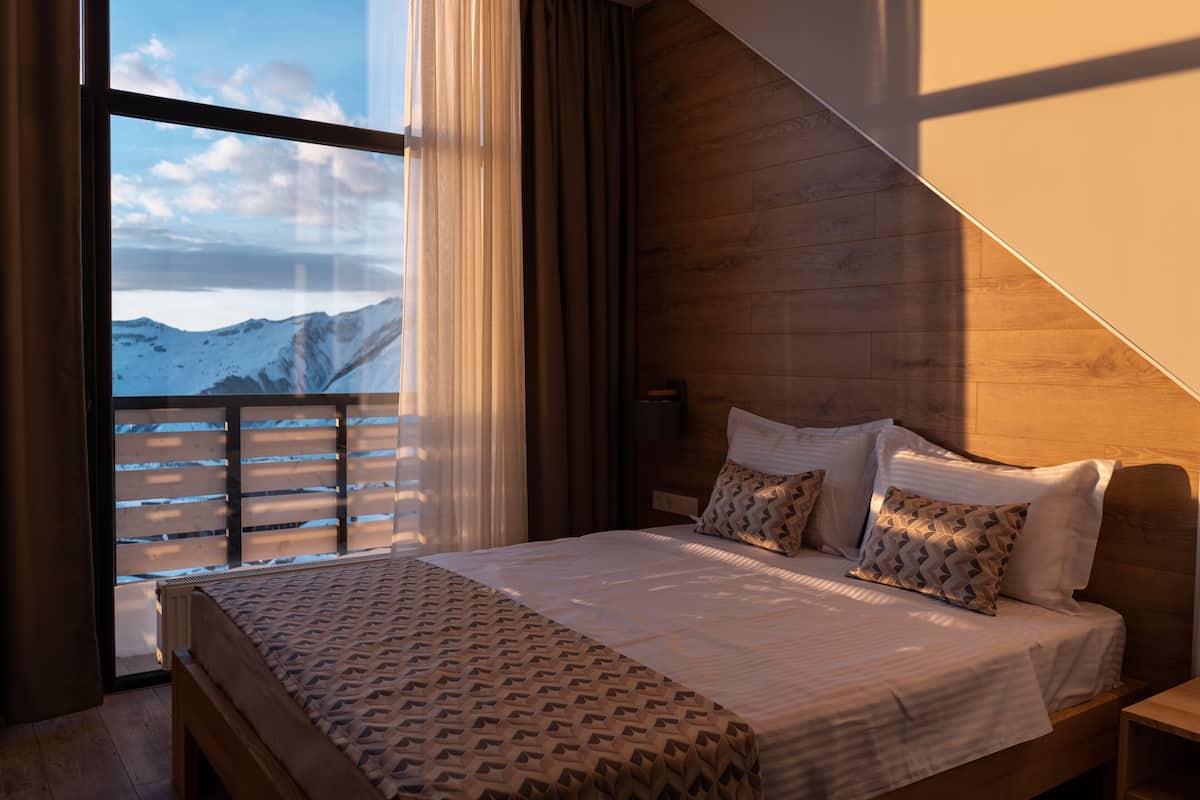 Un dormitorio con un ventanal grande, cabecera de madera y colcha estampada.