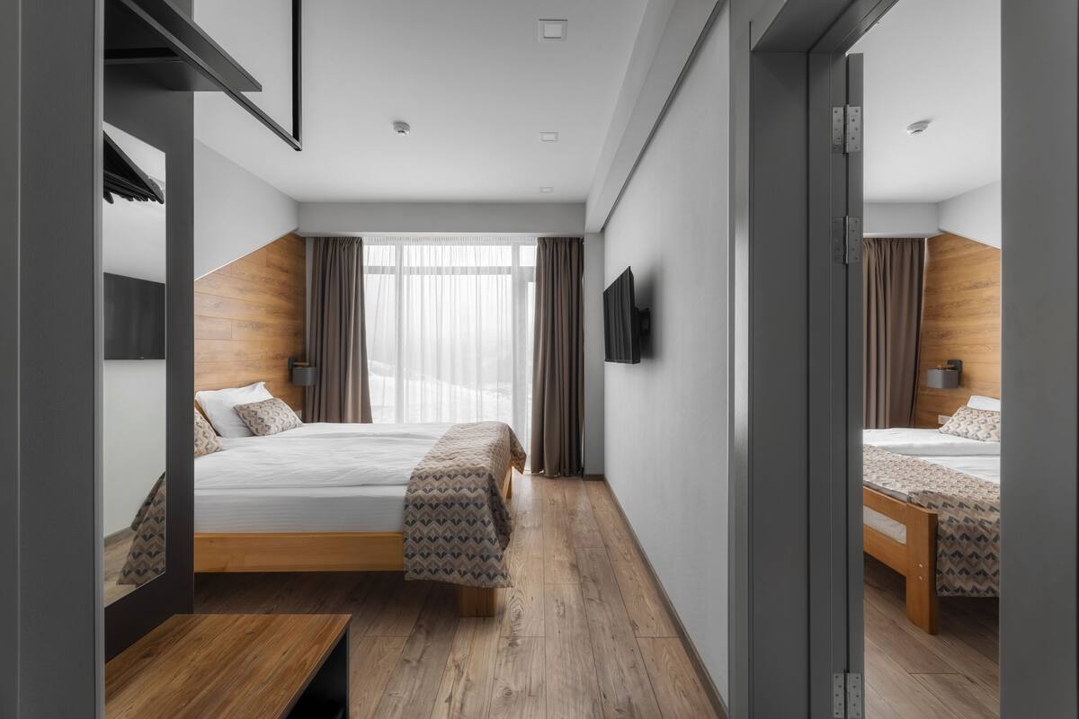 Una habitación de hotel moderna con suelo de madera, cama con cubrecama estampado, mesita de noche y televisión montada en la pared.