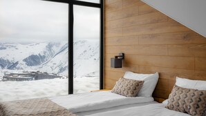 A bedroom with a large window, wooden headboard, and a bed with patterned pillows. - Gogi Resort (Kazbegi)