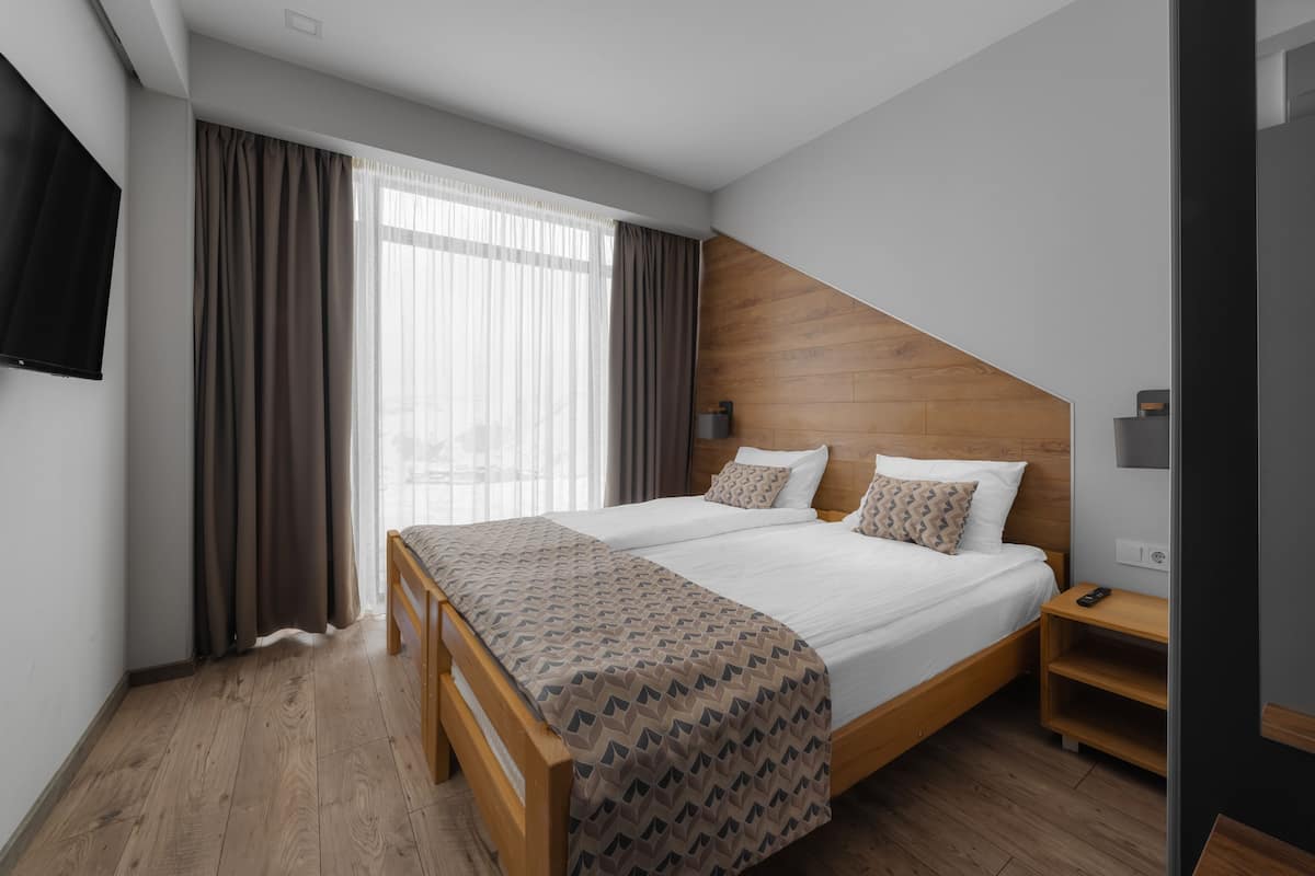 Una habitación de hotel moderna con una cama grande, cabecera de madera y televisión en la pared.