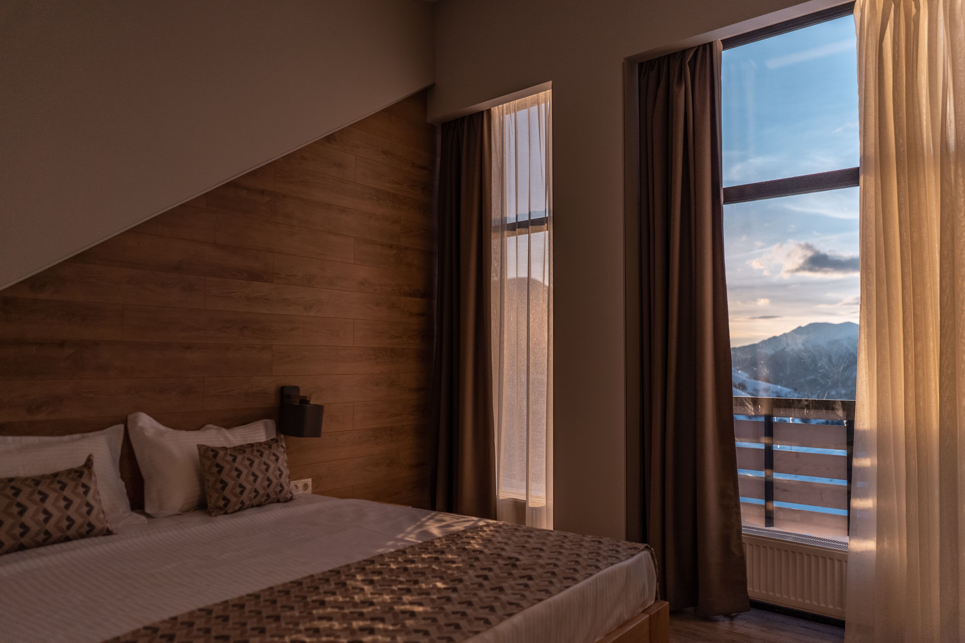 A bedroom with a large bed, wooden headboard, and a view of mountains through a window.