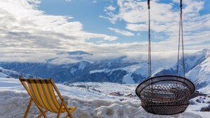 A wooden chair and a hanging chair overlooking a snowy mountain landscape. - Gogi Resort (Kazbegi)