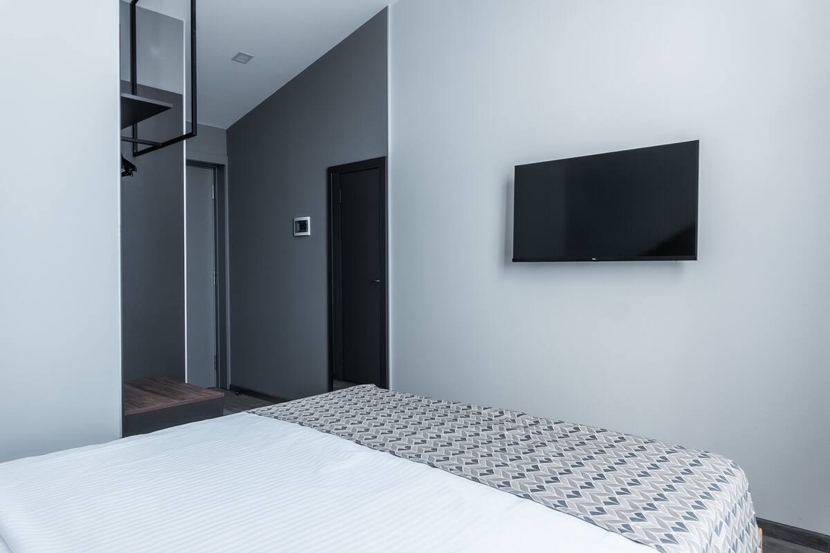 Un dormitorio moderno con una cama, un televisor montado en la pared y una puerta que da a otra habitación.