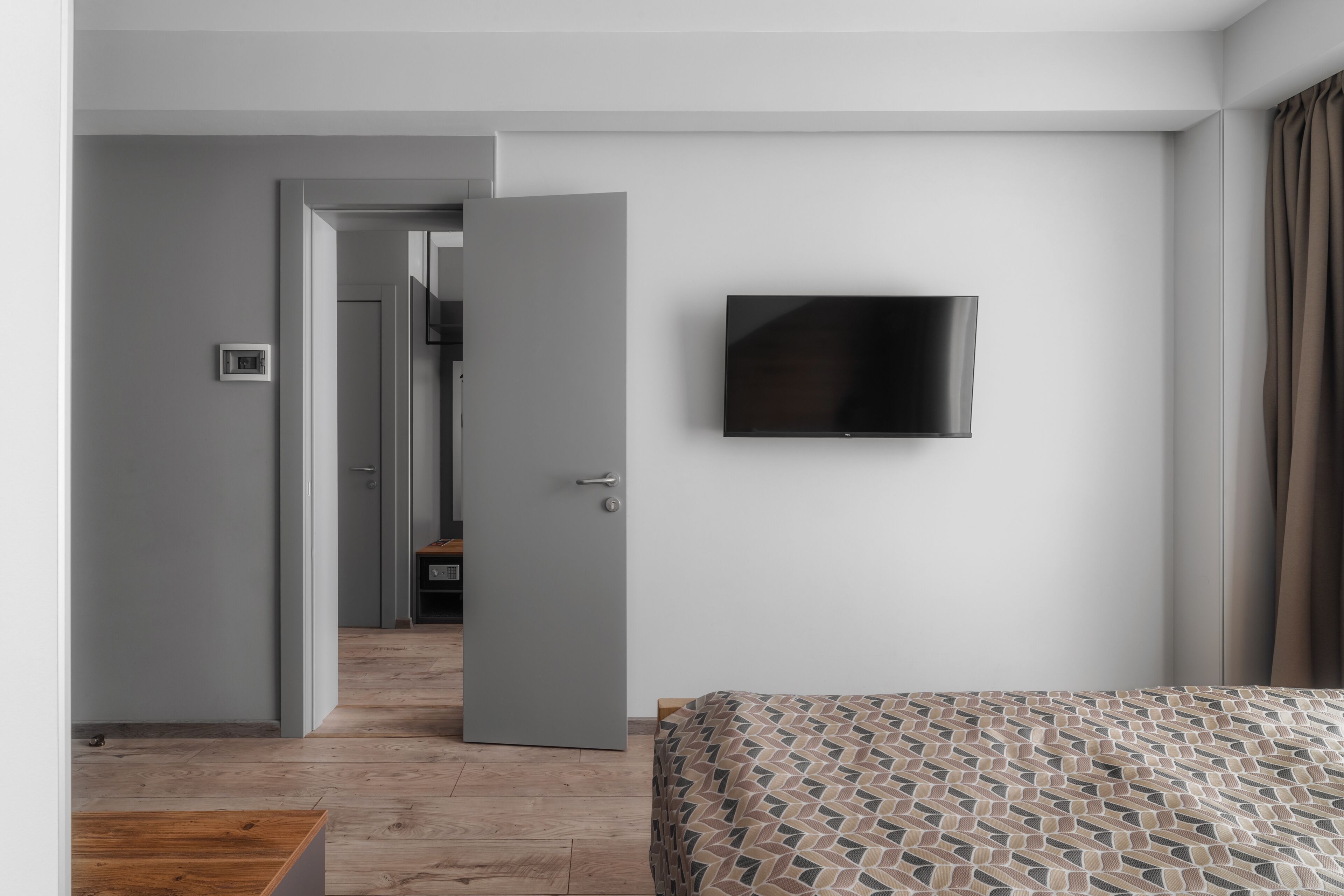 Una habitación de hotel con una cama, un televisor en la pared y una puerta que da a otra habitación.