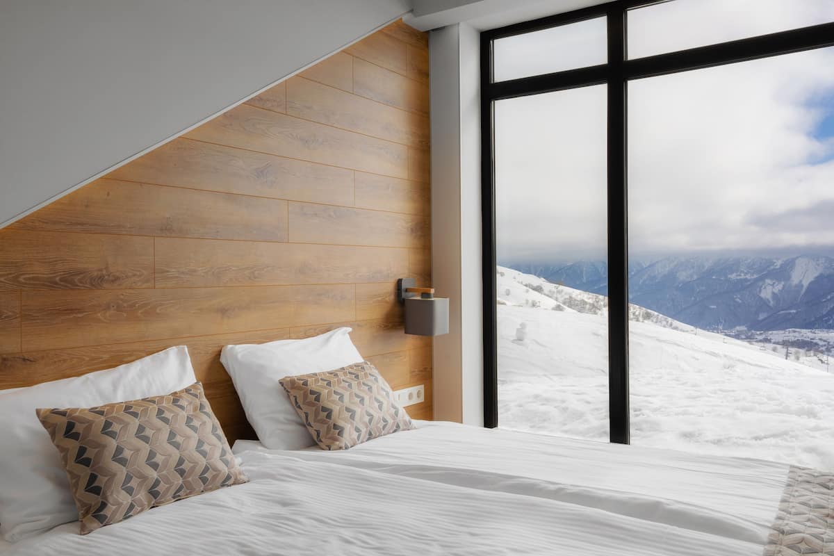 Un dormitorio con cabecera de madera, un ventanal con vistas a la montaña y dos almohadas estampadas.