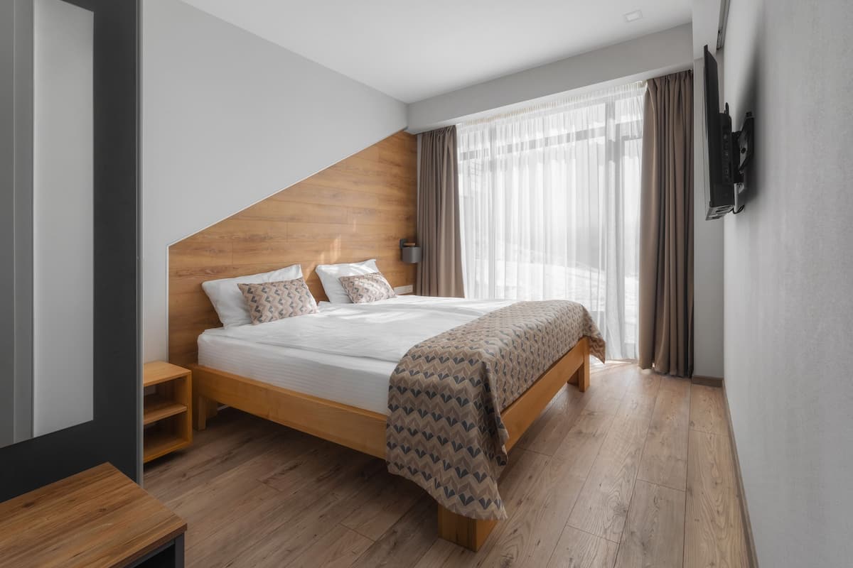 Un dormitorio moderno con cabecera de madera, una cama grande con ropa de cama estampada, una mesita de noche y un televisor montado en la pared.