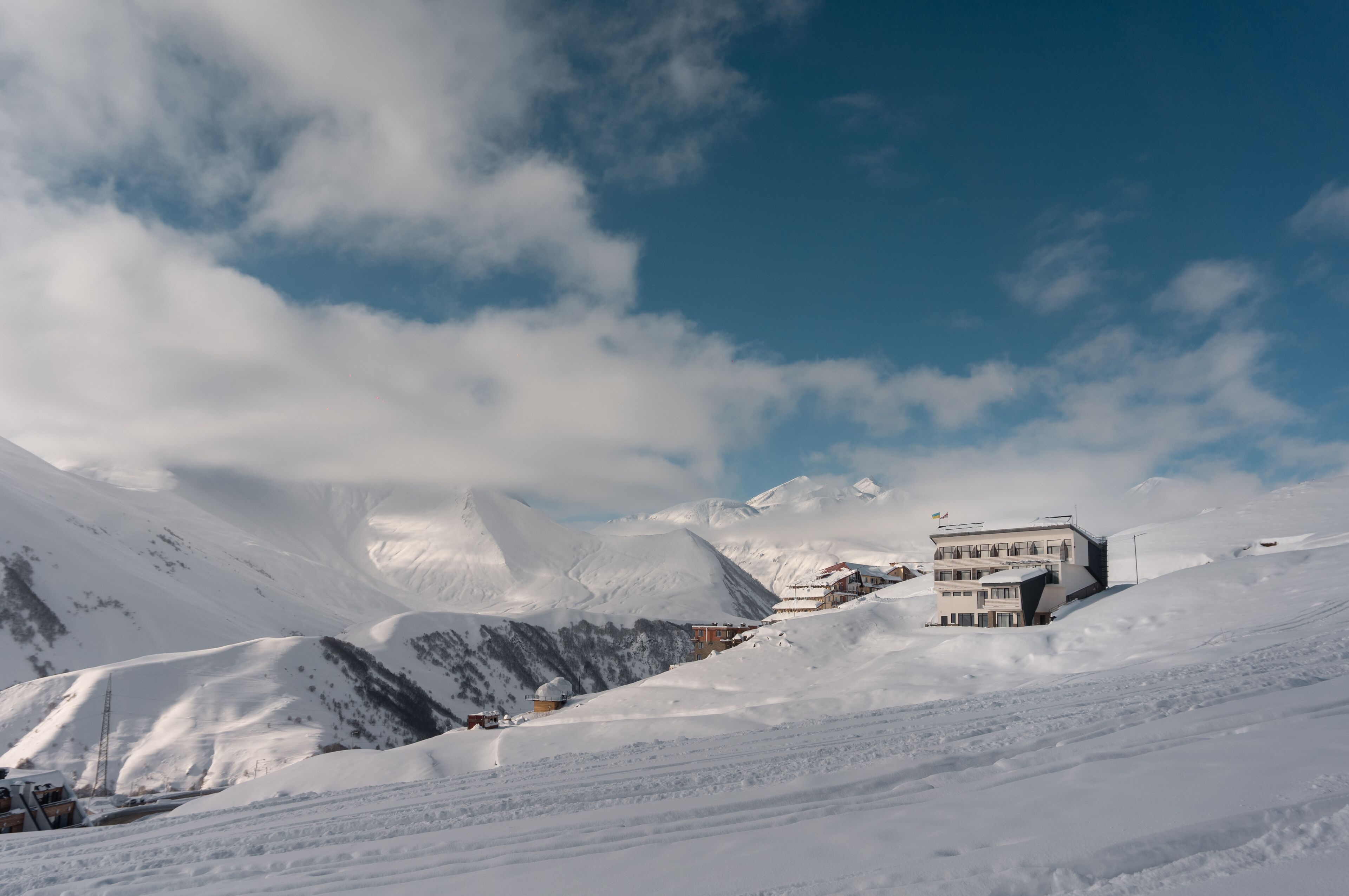 Paisaje nevado de una montaña con un edificio que tiene varios balcones y un teleférico al fondo.