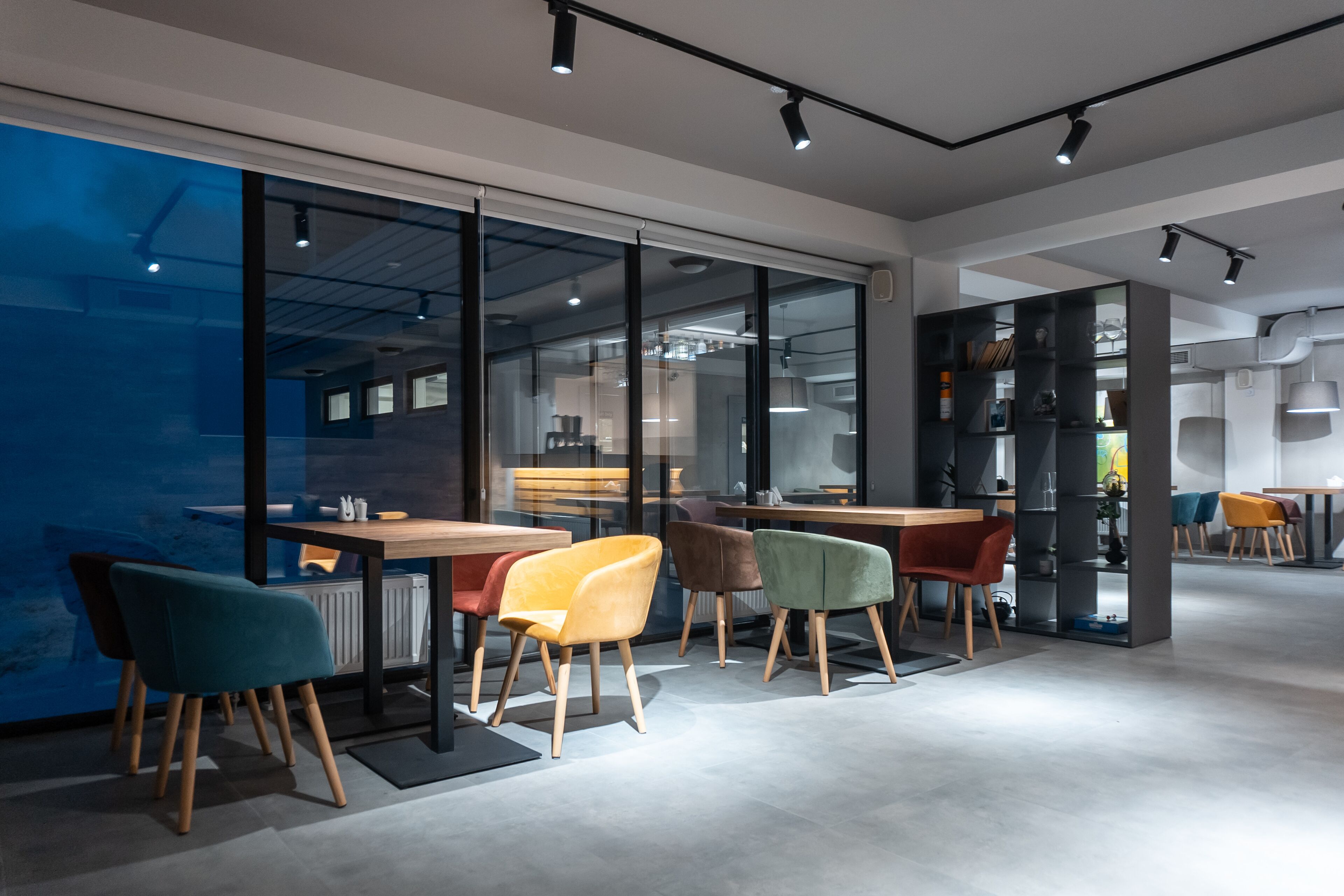 Un intérieur moderne avec des murs en verre, des tables en bois et des chaises colorées.