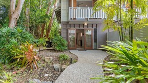 Une maison à deux étages dotée d’un espace extérieur aménagé et couvert, entourée d’une végétation luxuriante et d’arbres.