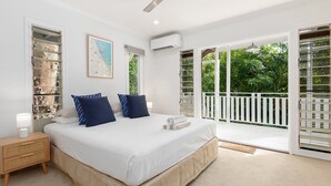 Une chambre avec un grand lit, une table de chevet, un tableau encadré et une vue sur la verdure à travers les portes du balcon.