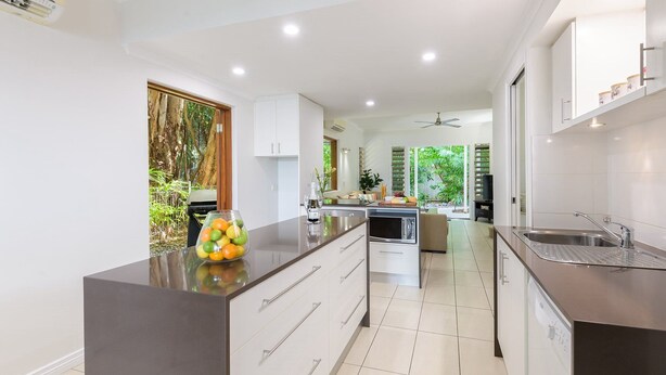 Une cuisine moderne dotée d’un îlot central, de meubles blancs et offrant une vue sur un jardin luxuriant.