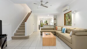 Un salon moderne avec un escalier, un ensemble de canapés, une table basse en bois et un ventilateur de plafond.