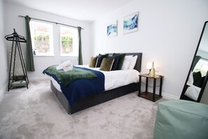 A bedroom with a bed, a bedside table with a bottle, a hanging clothes rack, and two windows with curtains. - 2 bed Cardiff City Centre Apartment Just Renovated (Cardiff)