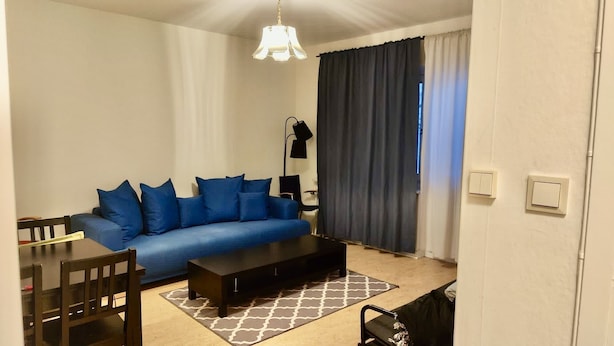 A living room with a blue sofa, a coffee table, a lamp, and a dining area with chairs and a table. - 2 Room Apartment in Hammarby by Stockholm City (Johanneshov)