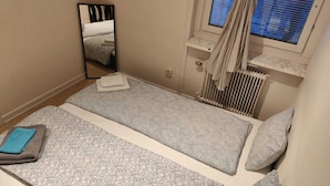 A small, single-bed room with a patterned bedspread, a mirror, a radiator, and a window with blinds. - 2 Room Apartment in Hammarby by Stockholm City (Johanneshov)