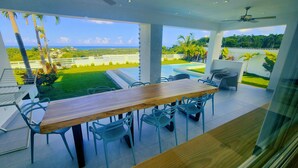 A modern outdoor dining area with a wooden table and chairs, overlooking a swimming pool and lush greenery. - Sunset Villa with Infinity Pool (Las Terrenas)