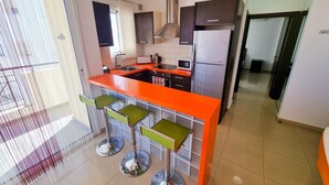 A modern kitchen with a central island, stainless steel appliances, and green bar stools. - City Vibrance Apartment (Larnaca)