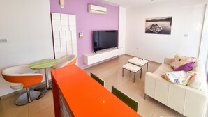 A modern living room with a flat-screen TV, a sofa, a chair, and a small table. - City Vibrance Apartment (Larnaca)