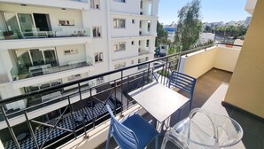 A balcony with a table and chairs, a checkered floor, and a view of a multi-story building with balconies. - City Vibrance Apartment (Larnaca)