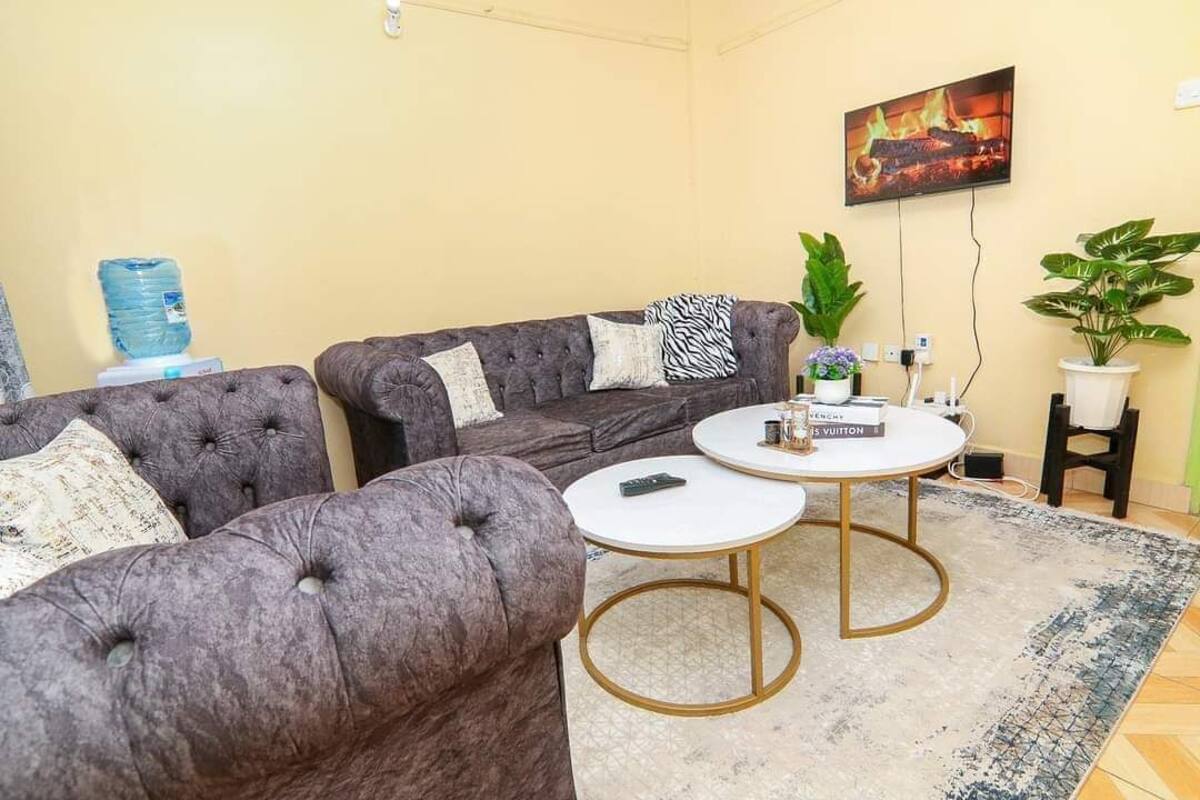 A living room with two tufted sofas, a round coffee table, and a flat-screen TV mounted on the wall.