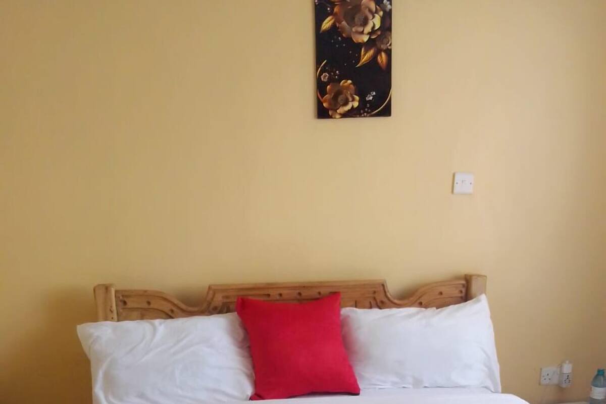 A bed with white and red bedding, a wooden headboard, and a floral artwork on the wall.
