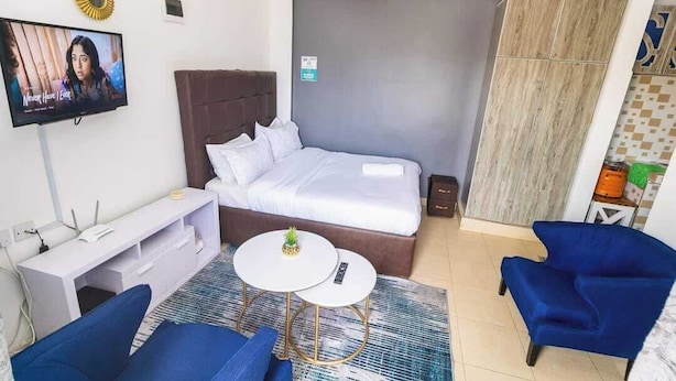 A hotel room with a bed, a TV, a desk, two chairs, and a small table. - Lux Suites Nairobi House Naivasha (Naivasha)