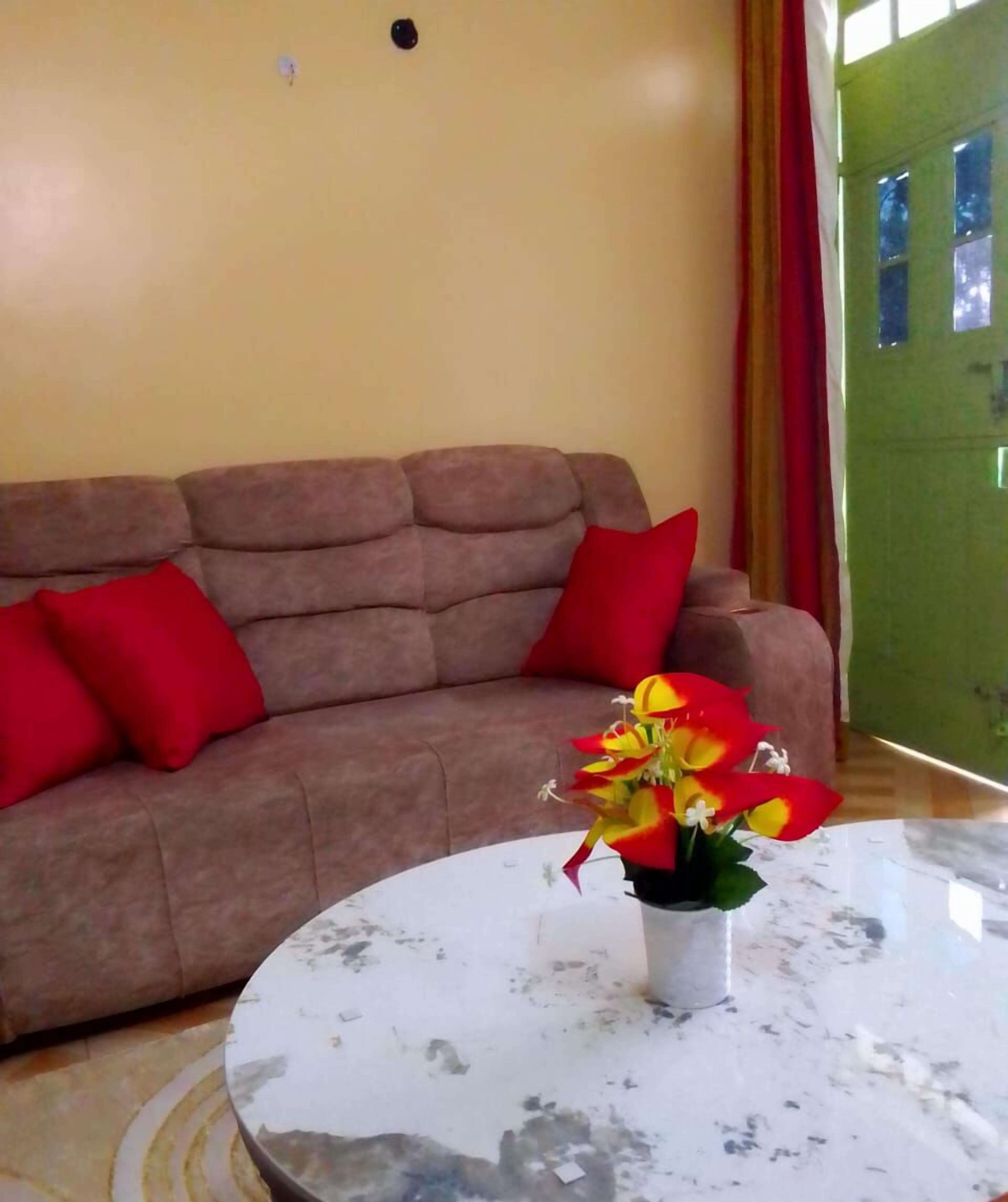 A living room with a brown sofa, red cushions, and a white marble coffee table with a flower vase.