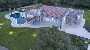 Ein modernes Haus mit Swimmingpool, überdachter Terrasse und gepflegtem Rasen.
