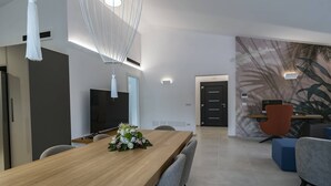Ein moderner Essbereich mit einem Holztisch, grauen Stühlen, einem Fernseher und einer Wand mit Palmblattmuster.